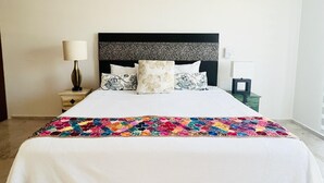 A neatly made bed with a white bedspread and a colorful quilt, a black headboard, and a bedside table with a lamp. - Modern 1 BR + Pool. Heart of Downtown (Isla Mujeres)