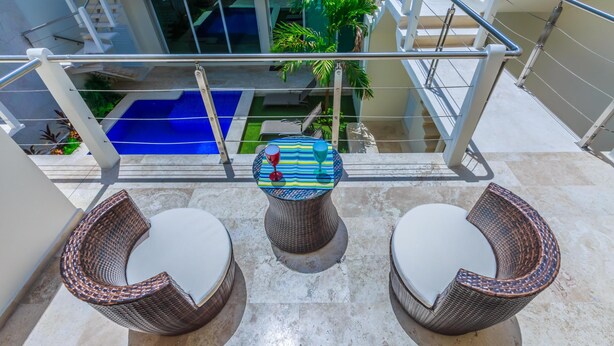 A balcony with wicker chairs and a table, overlooking a pool and a garden. - Modern 1 BR + Pool. Heart of Downtown (Isla Mujeres)