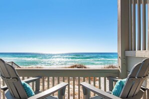 Una terraza de madera con dos sillas Adirondack mirando una playa y vistas al océano.