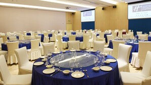 Une salle de conférence avec des tables rondes, des chaises blanches et des nappes bleues.