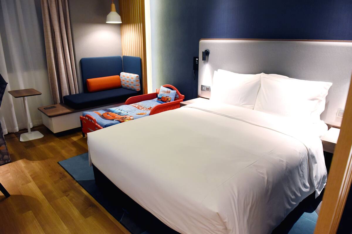 Ein Hotelzimmer mit einem großen Bett, einem Sofa mit orangenen Kissen, einem kleinen Tisch und einem Nachttisch.