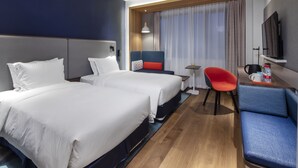Une chambre d’hôtel avec deux lits, un bureau, une chaise, une télévision et une fenêtre avec des rideaux.