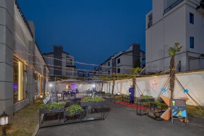 Een terras met tafels en stoelen, lichtjes en een bar met een neonreclame.