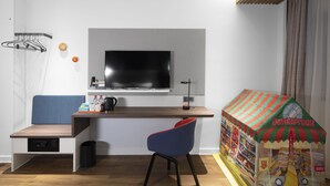 Une chambre d’hôtel moderne équipée d’une télévision, d’un bureau avec une chaise, d’un petit coin salon et d’une maisonnette pour enfants.