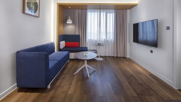 Un salon moderne avec un canapé bleu, une petite table ronde et un téléviseur à écran plat fixé au mur.