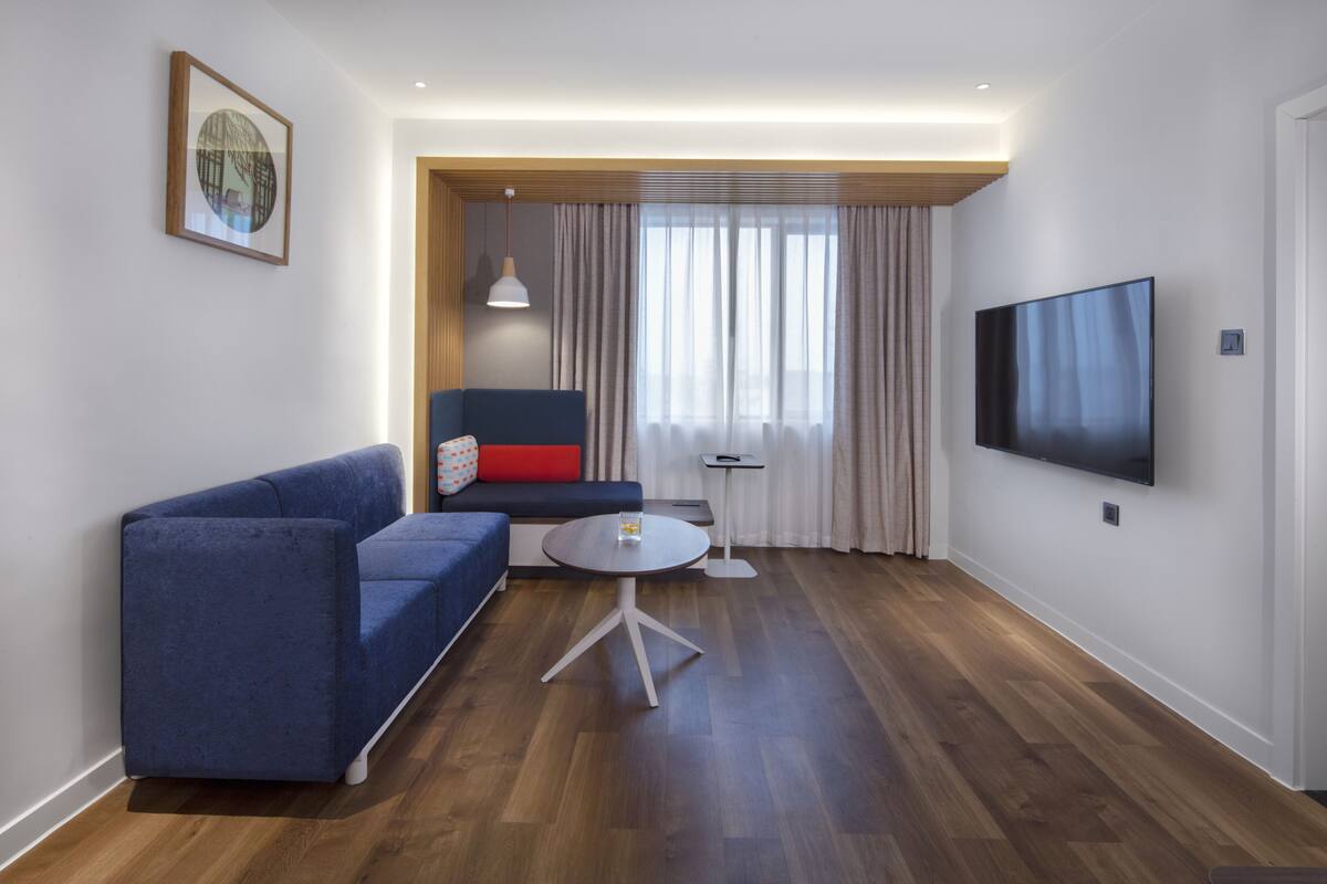 Ein modernes Wohnzimmer mit einem blauen Sofa, einem kleinen runden Tisch und einem an der Wand montierten Flachbildfernseher.
