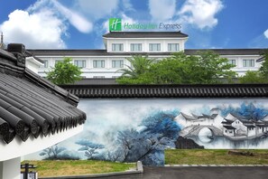 Un bâtiment de style traditionnel, agrémenté d’une enseigne moderne « Holiday Inn Express », d’une fresque représentant un paysage paisible et d’un toit traditionnel recouvert de tuiles.