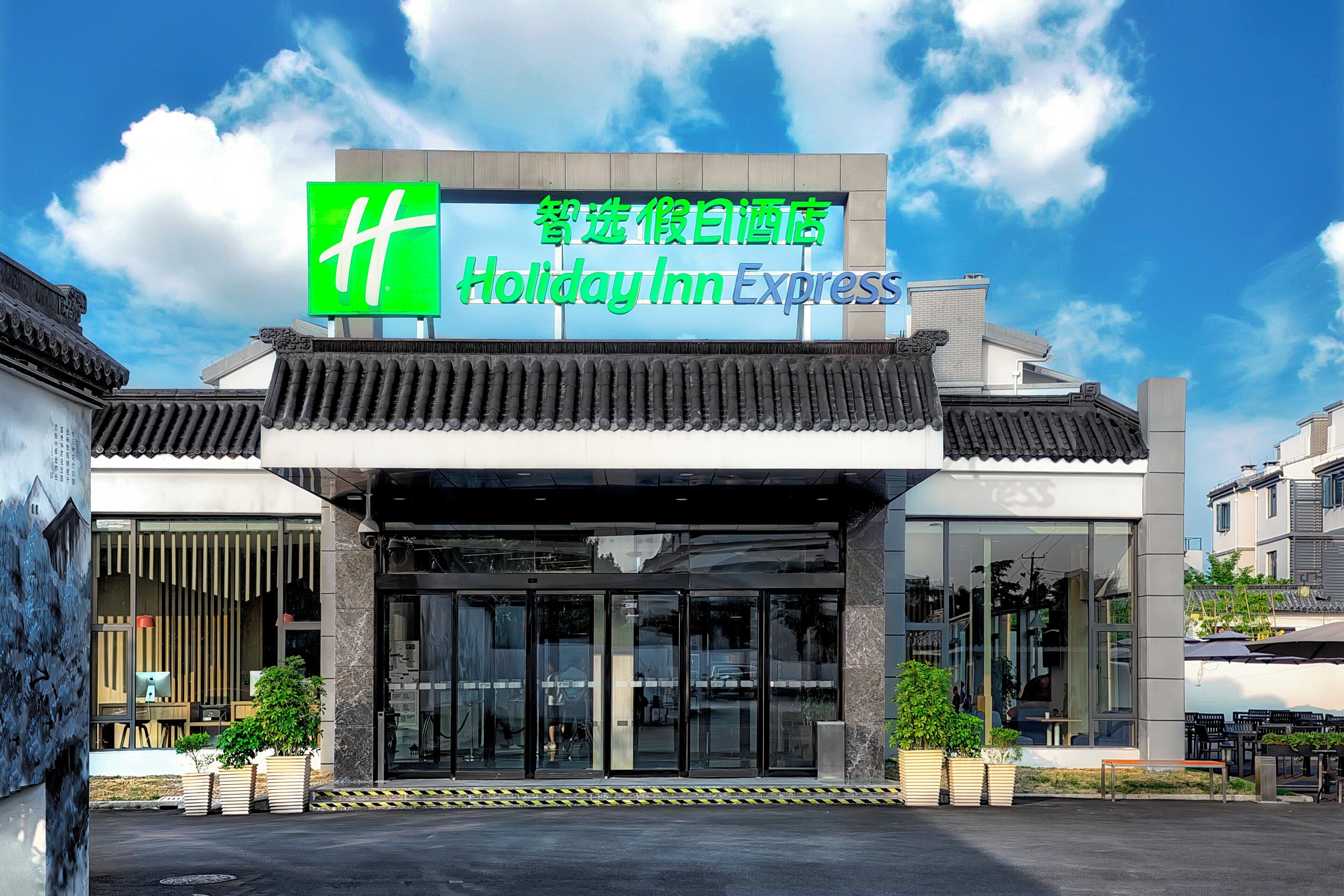 Un hotel Holiday Inn Express con fachada de arquitectura tradicional, un amplio acceso de vidrio y un cielo despejado.