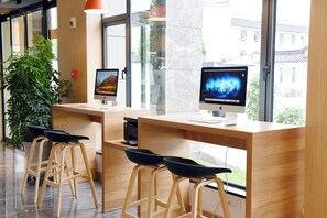 Un espace de travail moderne équipé de deux ordinateurs Apple iMac, de tabourets en bois et d’une grande plante en pot.