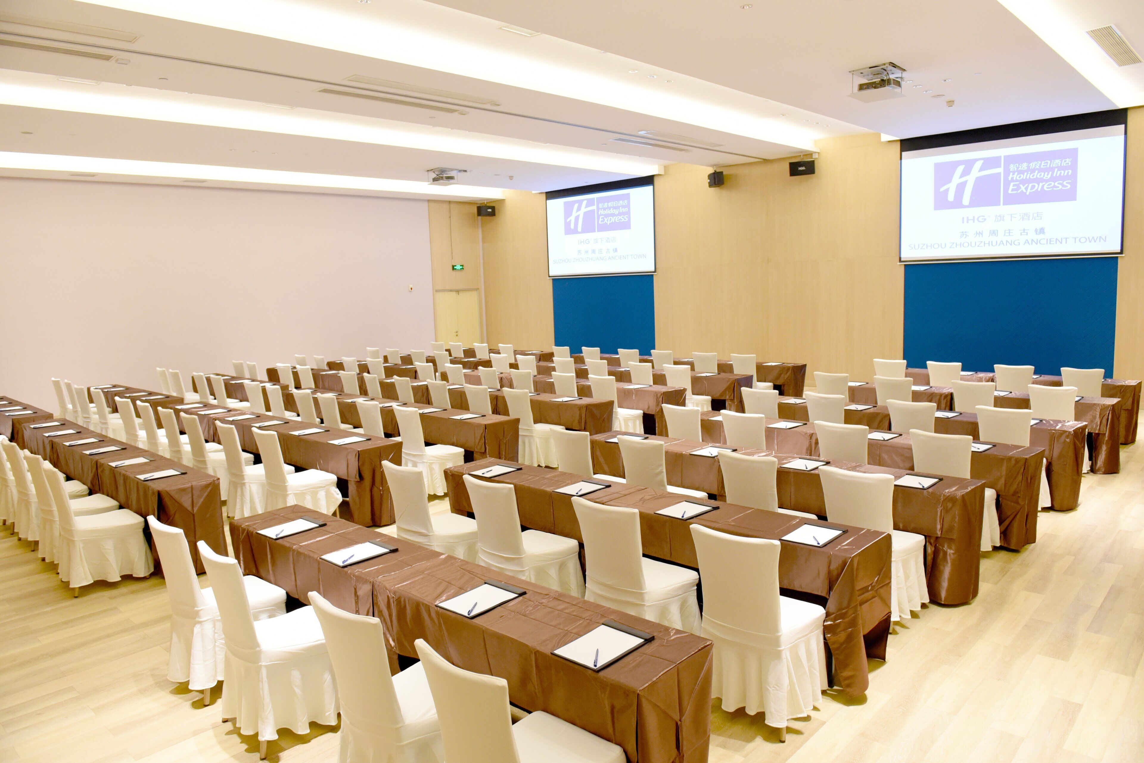 A conference room with rows of tables and chairs, a projector screen, and a blue accent wall.