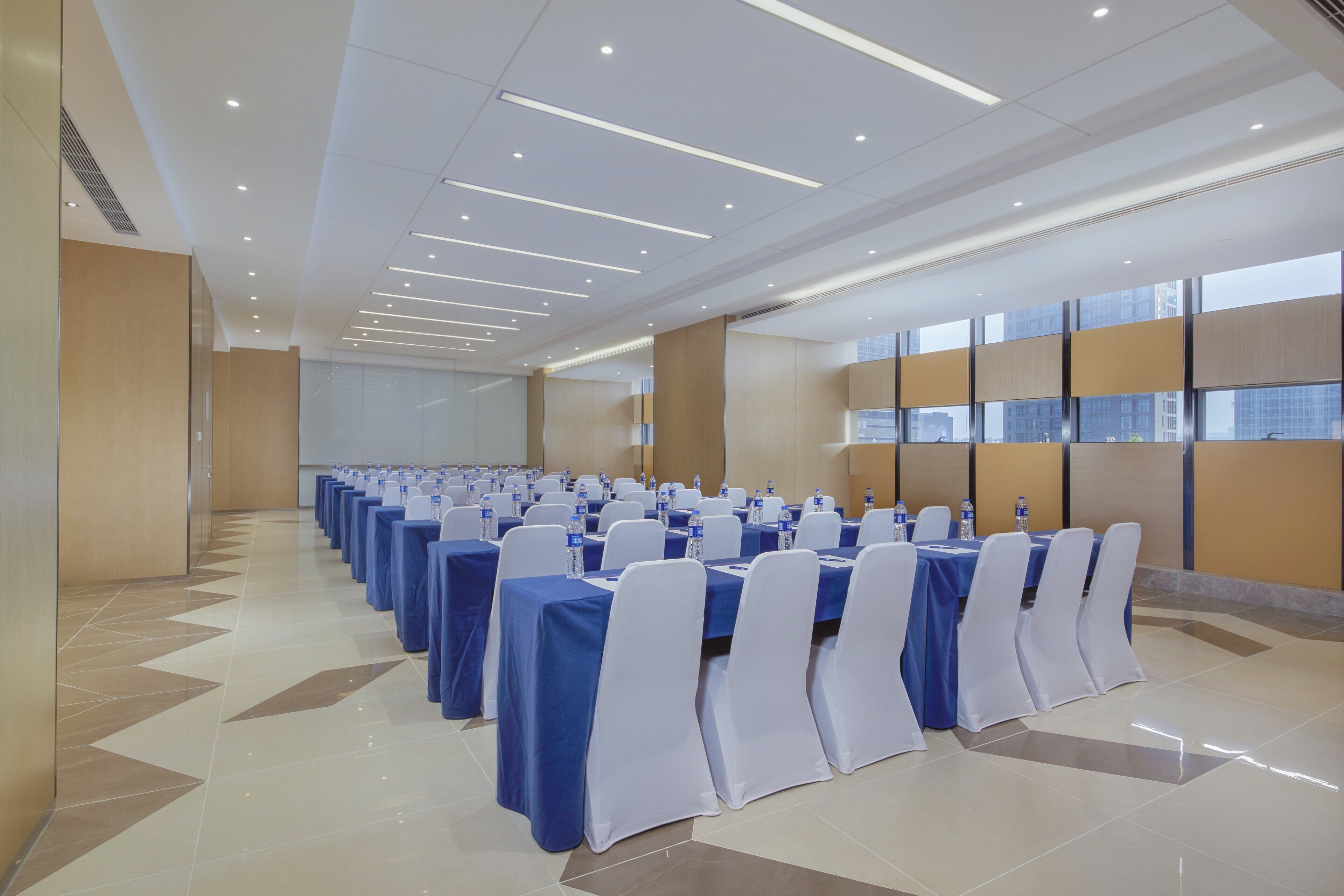 A conference room with rows of tables, white chairs, and blue tablecloths.