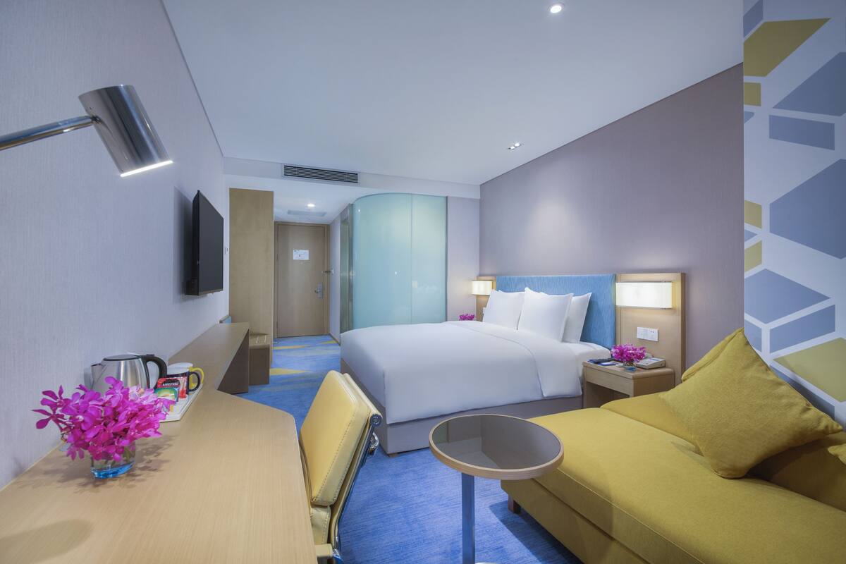 Une chambre d’hôtel comprenant un lit, un canapé, un bureau avec une lampe et un téléviseur fixé au mur.