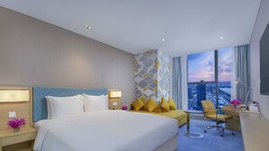 Een moderne hotelkamer met een groot bed, een bureau, een stoel en uitzicht op de stad door het raam.