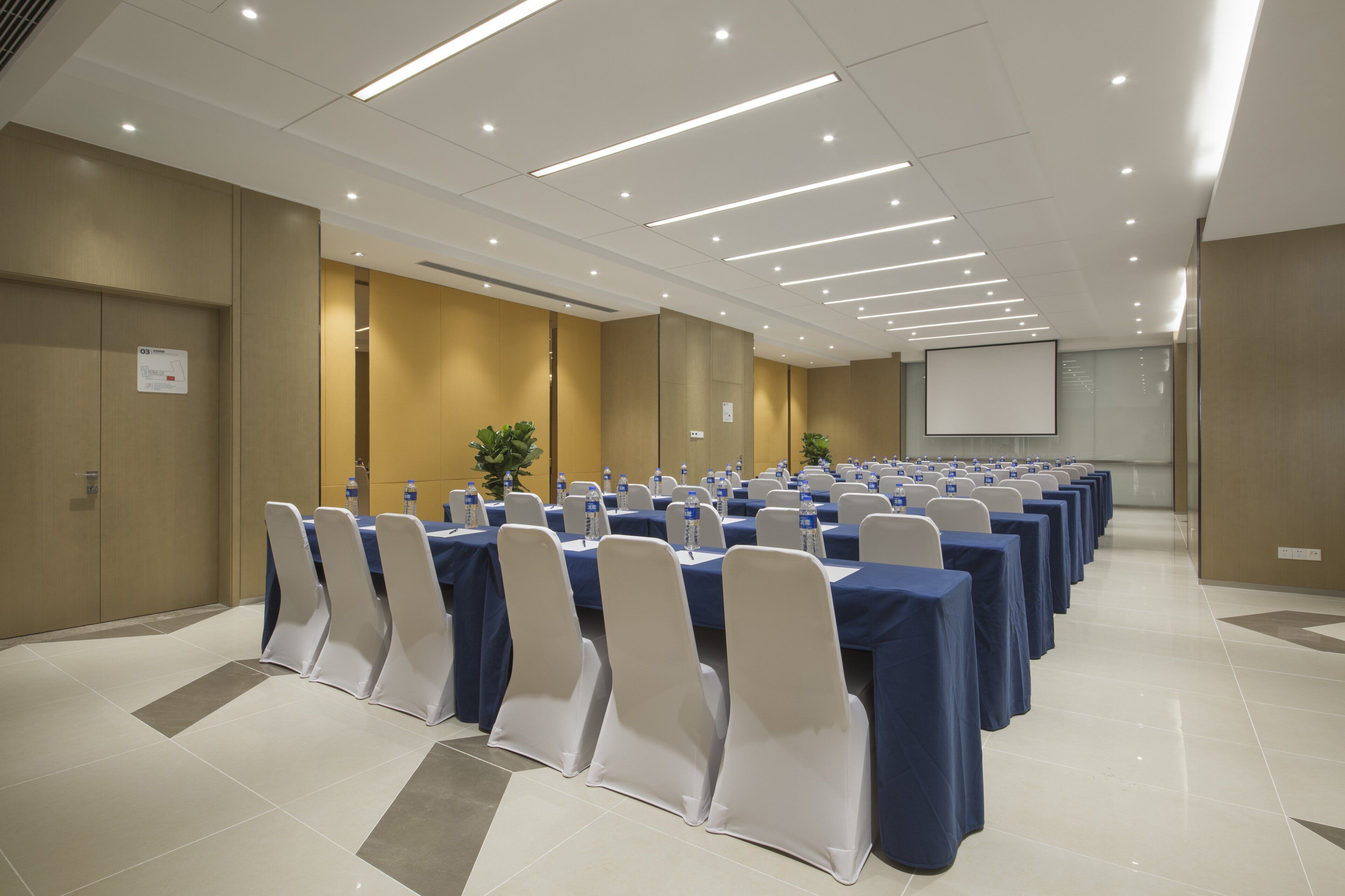 Un salón de conferencias con filas de mesas, sillas y botellas de agua.