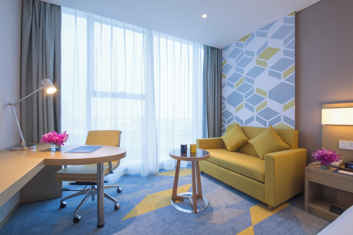 Quarto de hotel com escrivaninha, cadeira, sofá e uma pequena mesa.