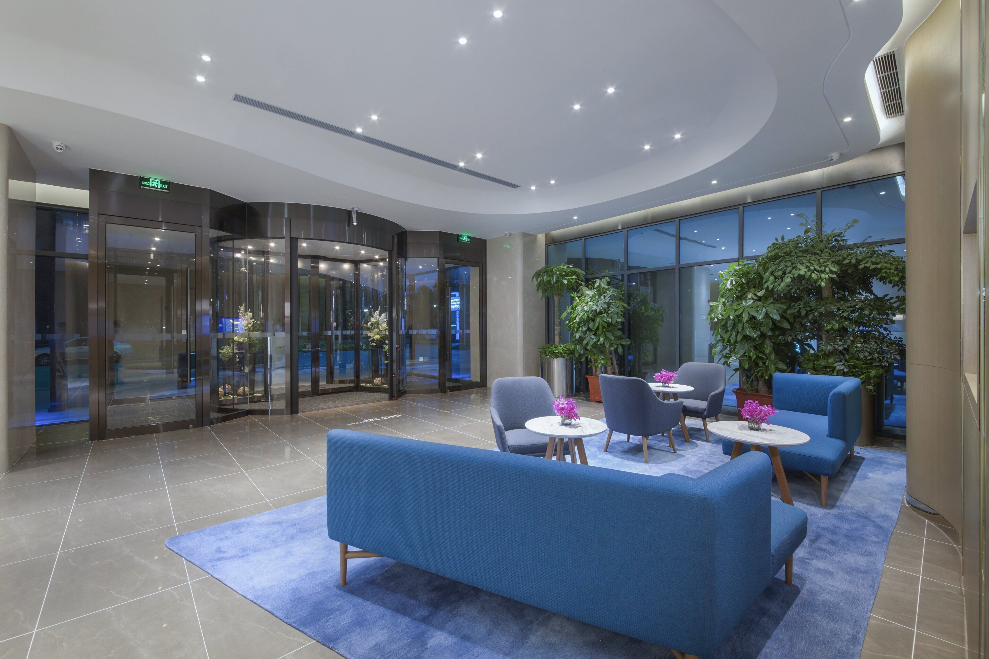 Eine Lobby mit einem blauen Sofa, runden Tischen und Topfpflanzen.