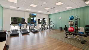 Un gimnasio con cintas de correr, elípticas y una banca para pesas.
