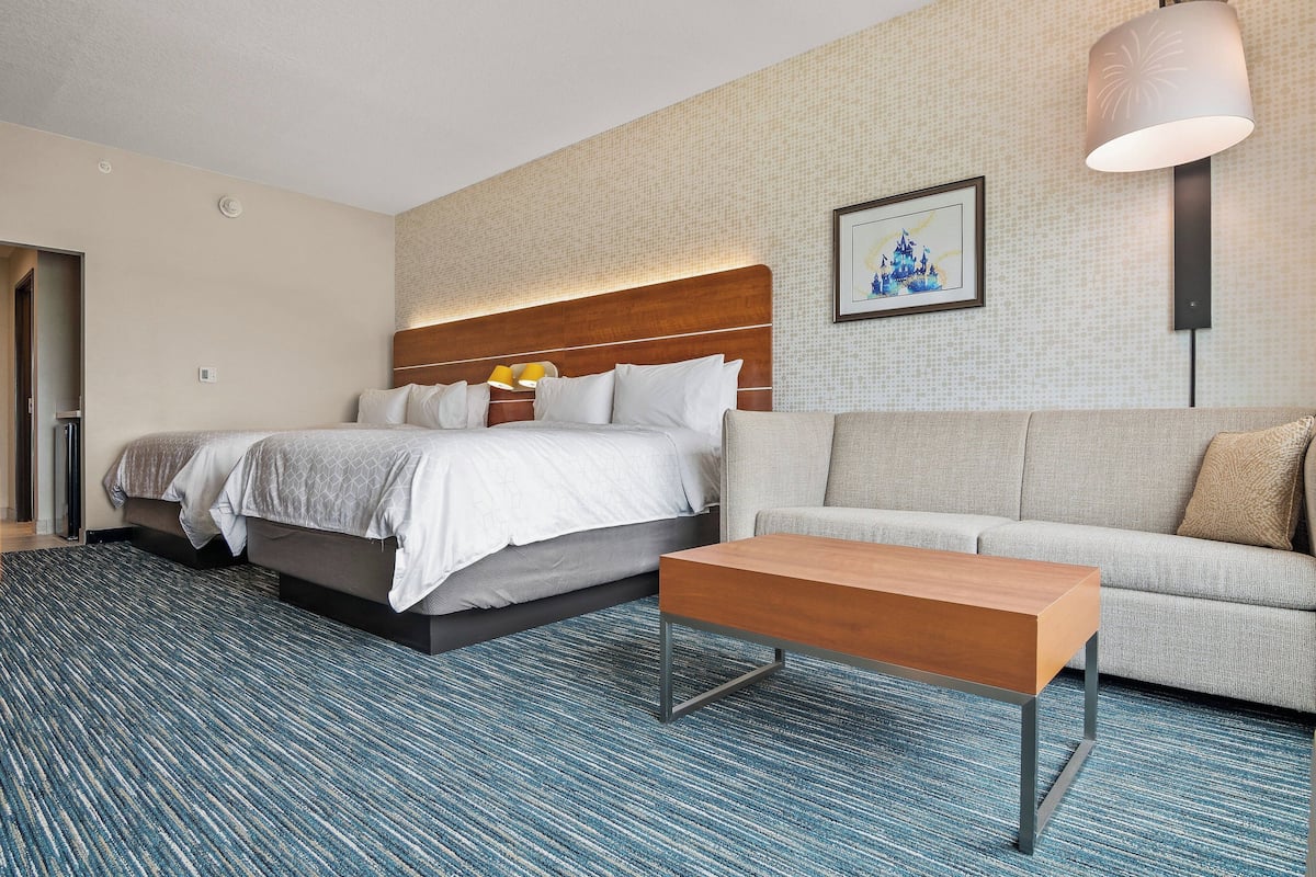 Ein Hotelzimmer mit einem großen Bett, einer Couch, einem Holztisch und einem gemusterten Teppich.