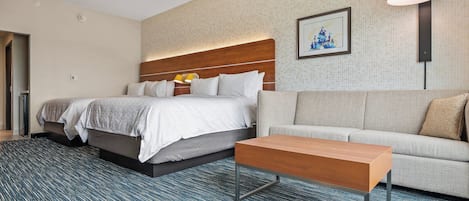 A hotel room with a large bed, a sofa, a wooden coffee table, and a patterned carpet.