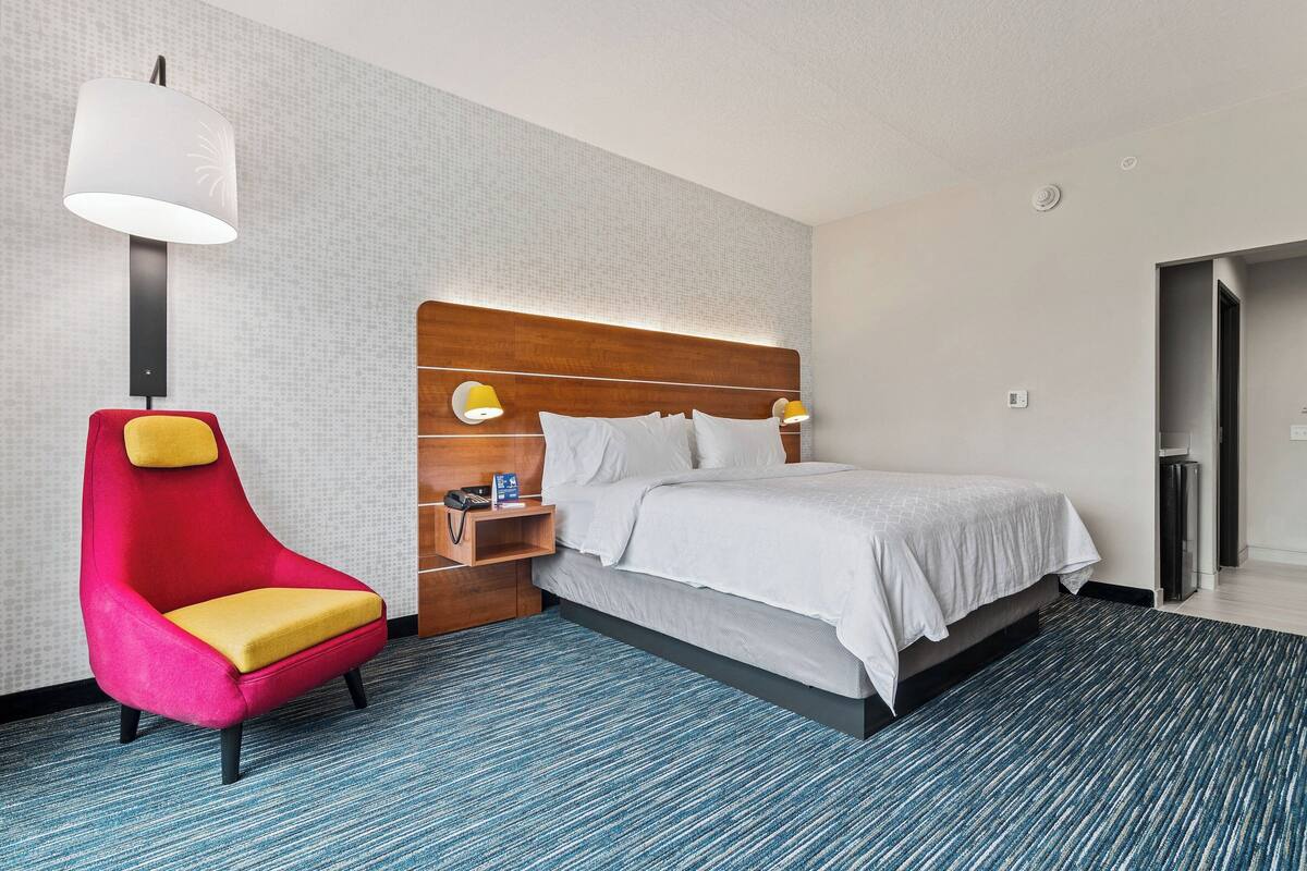 Ein Hotelzimmer mit einem Bett, einem roten und gelben Sessel, einem Nachttisch und einer Wandleuchte.