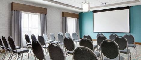 A conference room with rows of chairs, a projector screen, and a carpeted floor.
