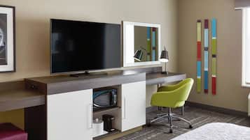 A hotel room with a flat-screen TV, a desk with a lamp, a green chair, a coffee maker, and a bed.