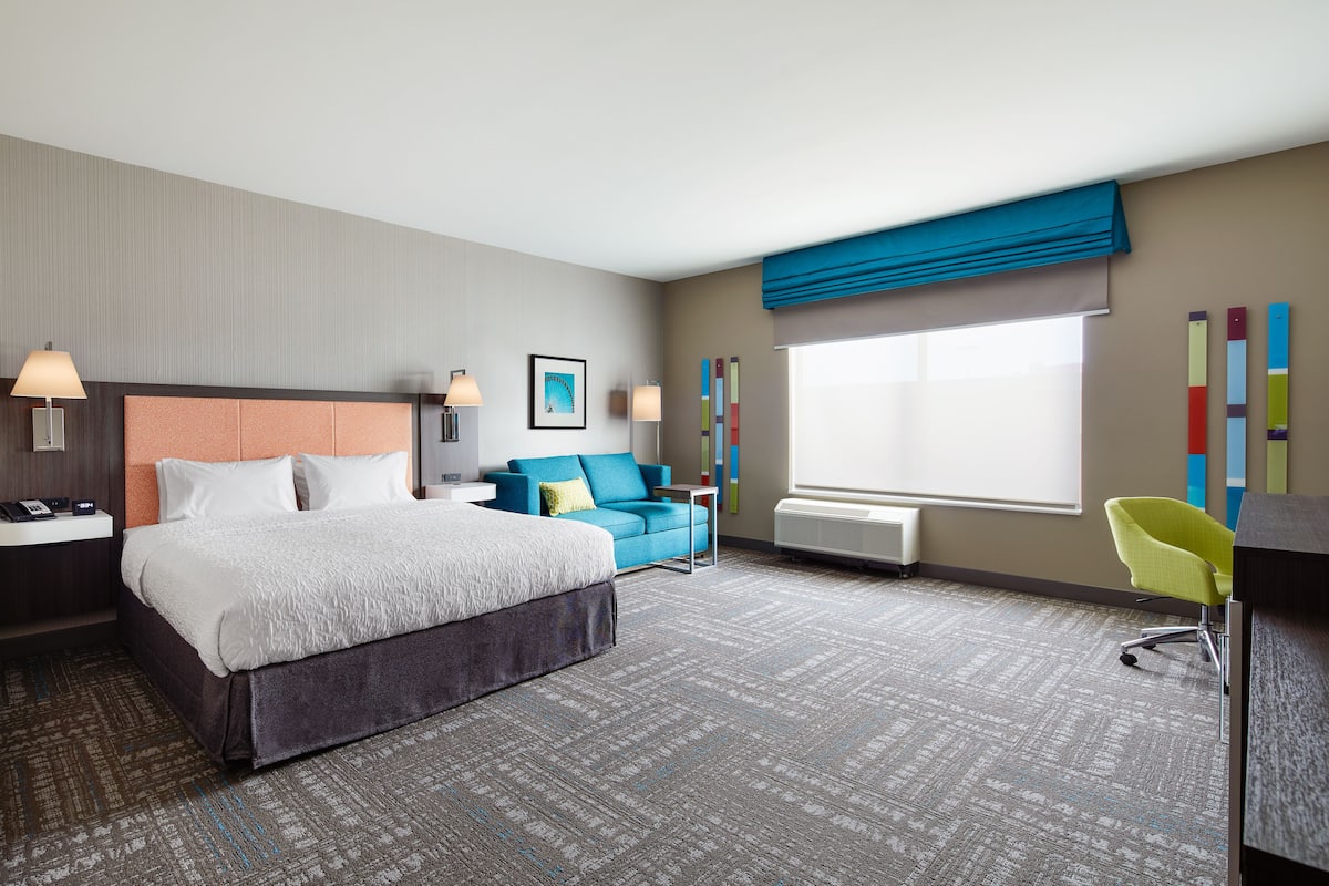 A hotel room with a large bed, a blue sofa, a desk, and a chair.