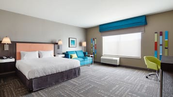 A hotel room with a large bed, a blue sofa, a desk, and a chair.