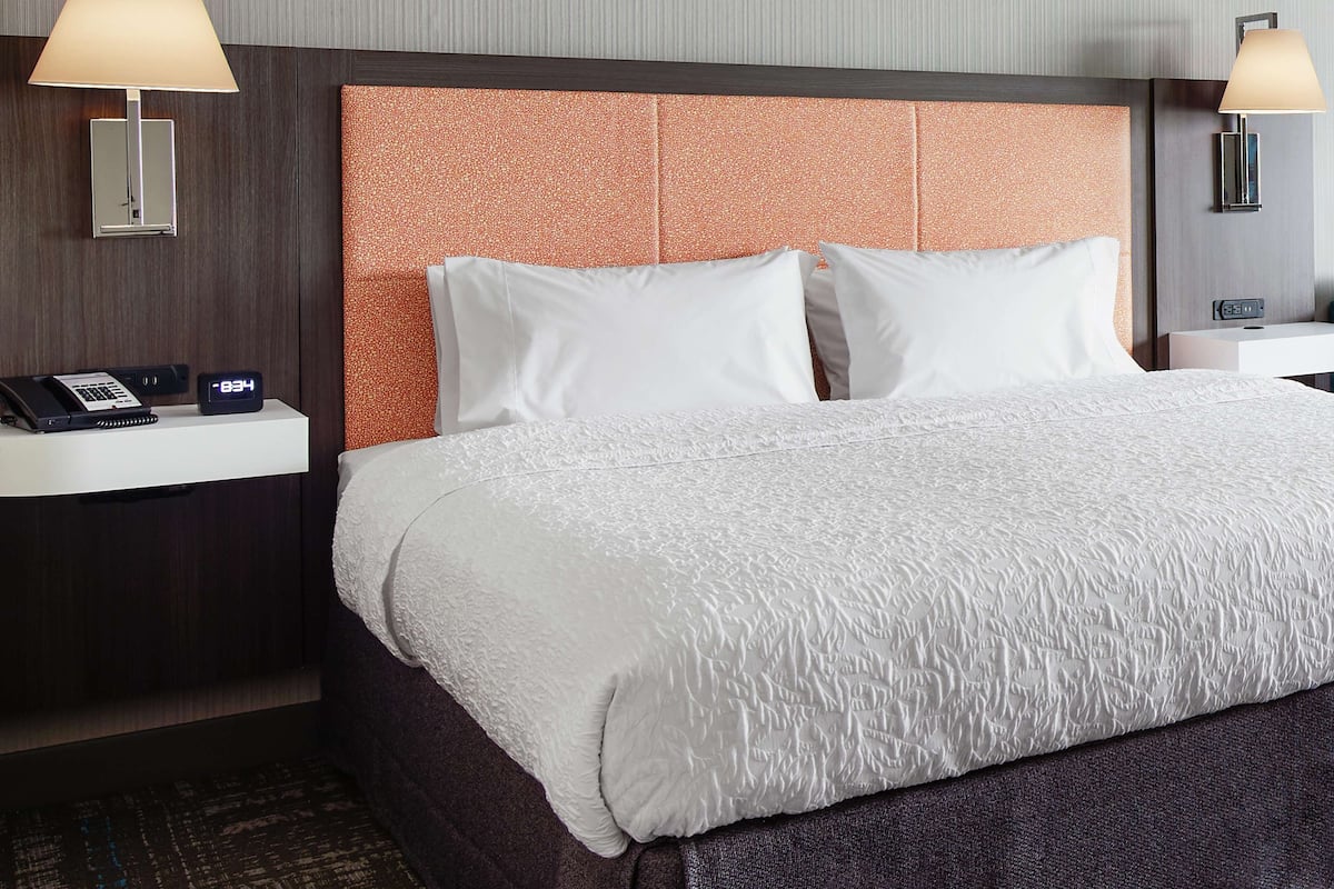 A hotel room with a large bed, two bedside tables, a nightstand, a clock, and a lamp on each side.