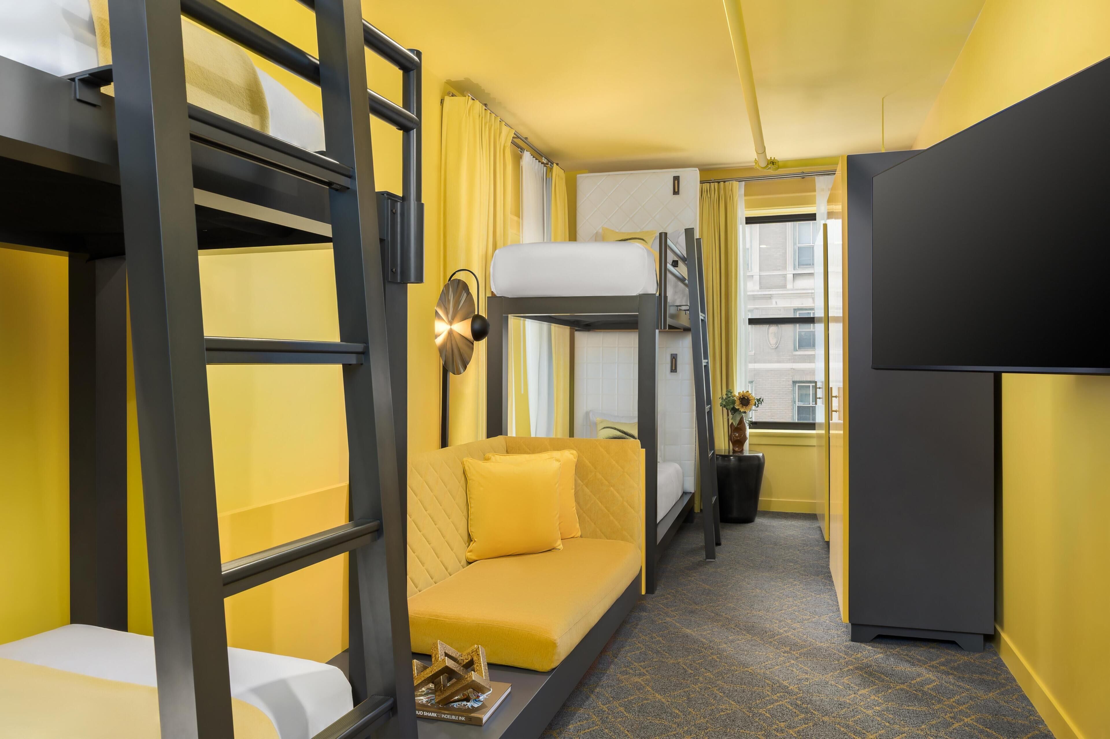 Habitación de hotel compacta con literas, sofá, escritorio y televisión.