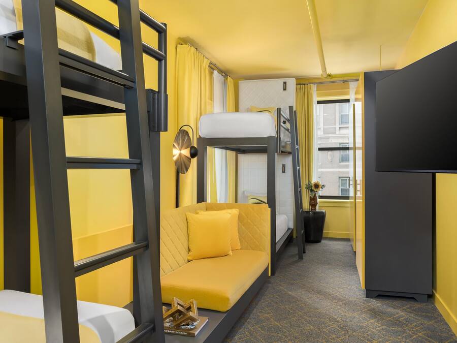A compact hotel room with bunk beds, a sofa, a desk, and a television.