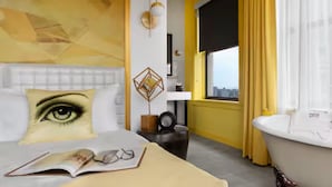 A modern hotel room with a large window, a bathtub, and a unique eye-themed pillow. - Angad Arts Hotel St. Louis, Tapestry Collection by Hilton (St. Louis)