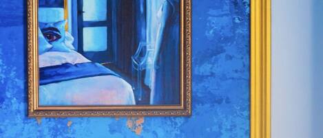 A painting of a room with a bed and a window, framed in gold, on a textured blue wall.