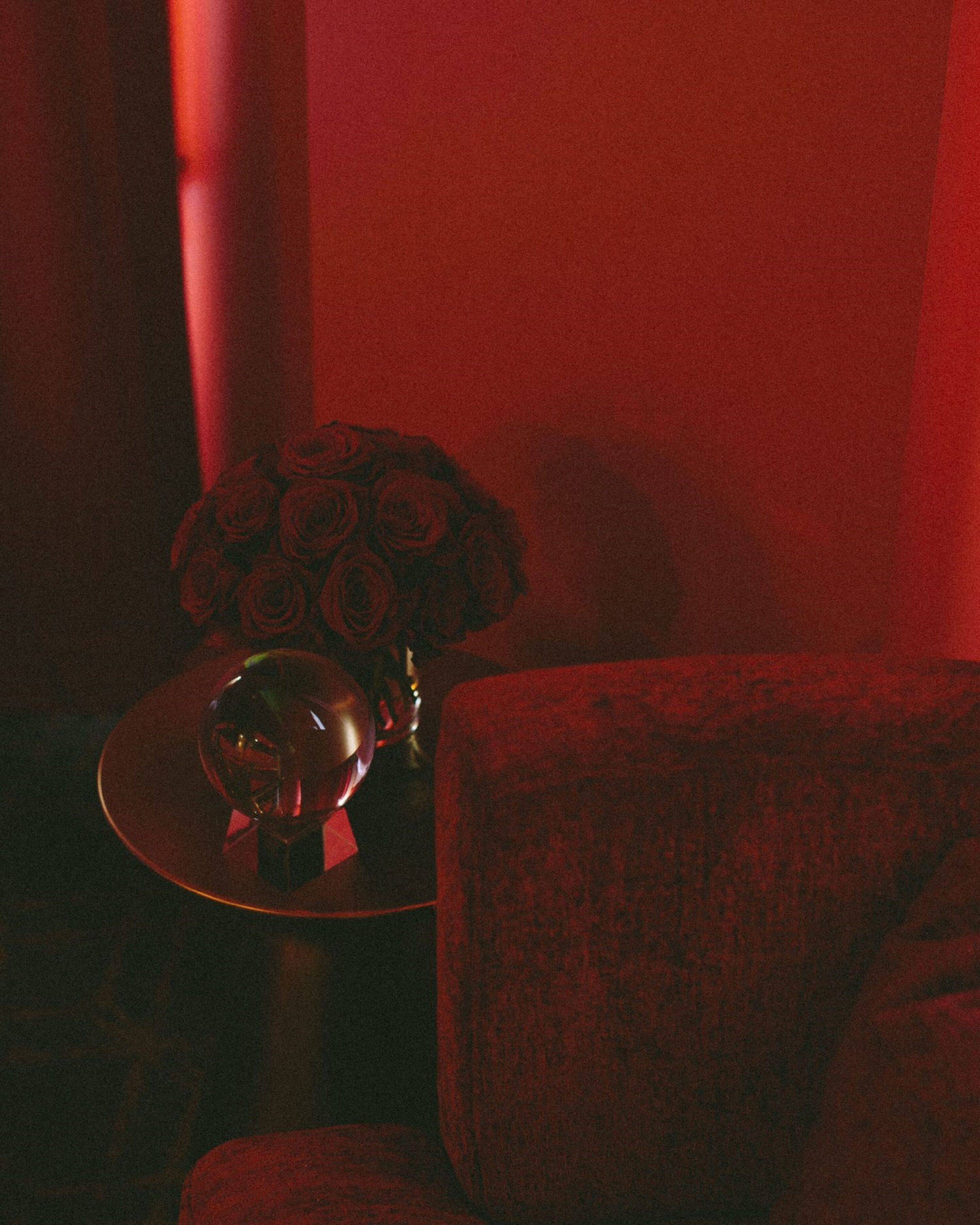 A dimly lit room with a red hue, featuring a table with a crystal globe and a bouquet of roses.