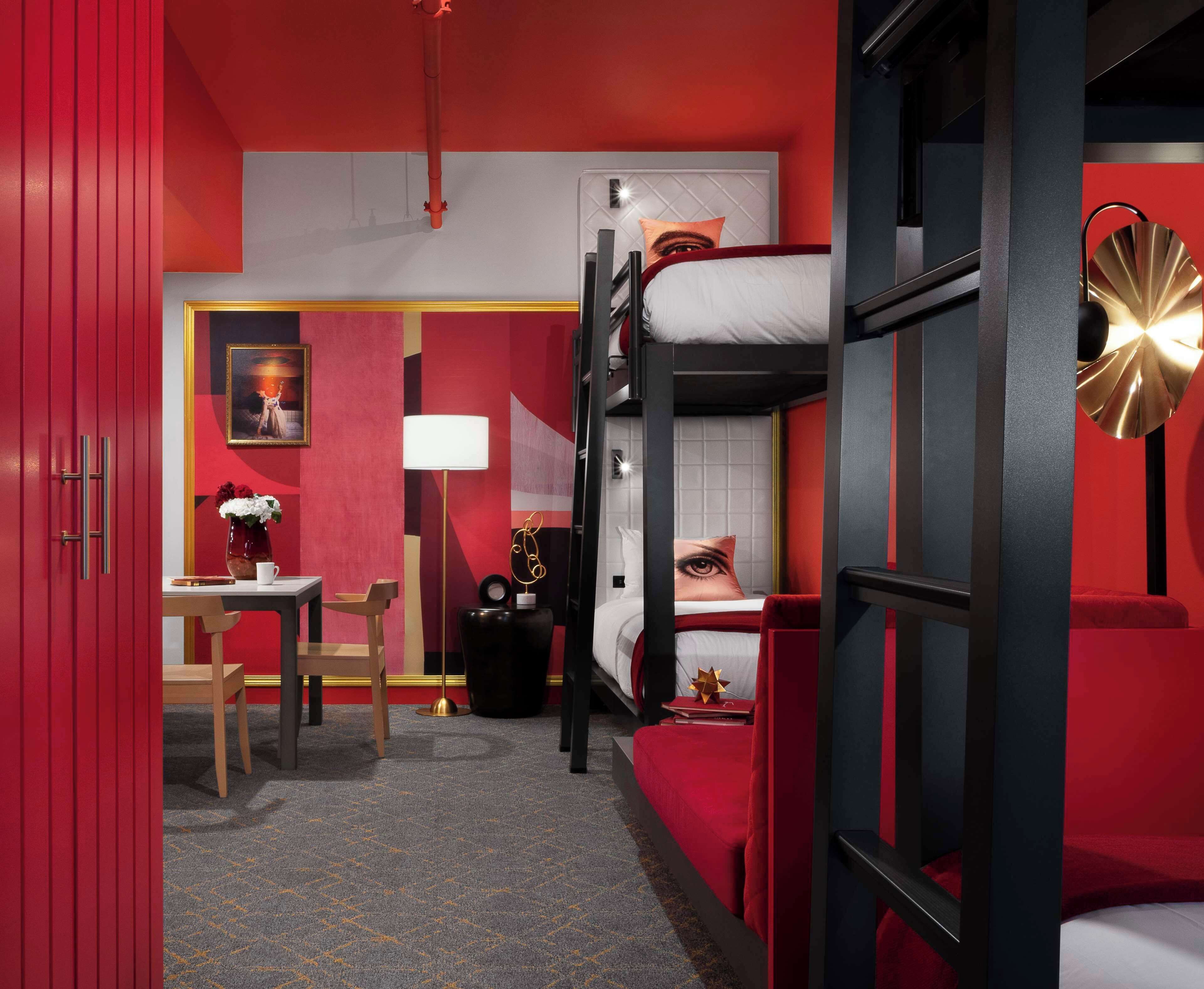 Een hotelkamer met een stapelbed, een bureau met stoel, een lamp en een schilderij aan de muur.