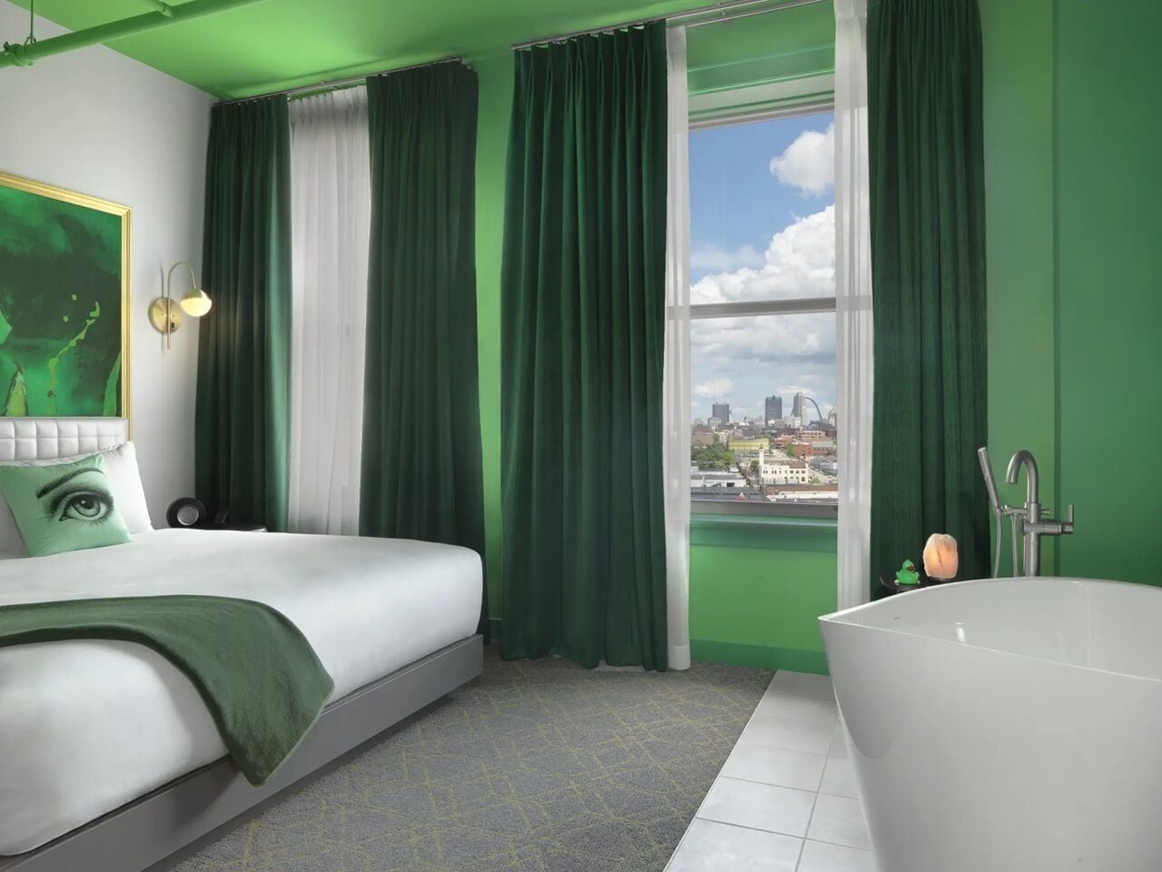 A modern hotel room with a large bed, a bathtub, and a city view through the window.