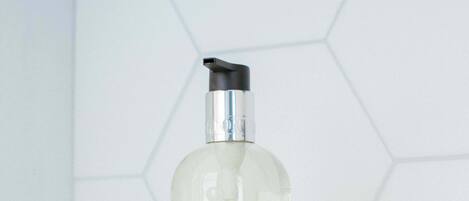 Una botella de jabón de manos Molton Brown sobre una superficie blanca con un salpicadero de azulejos hexagonales.