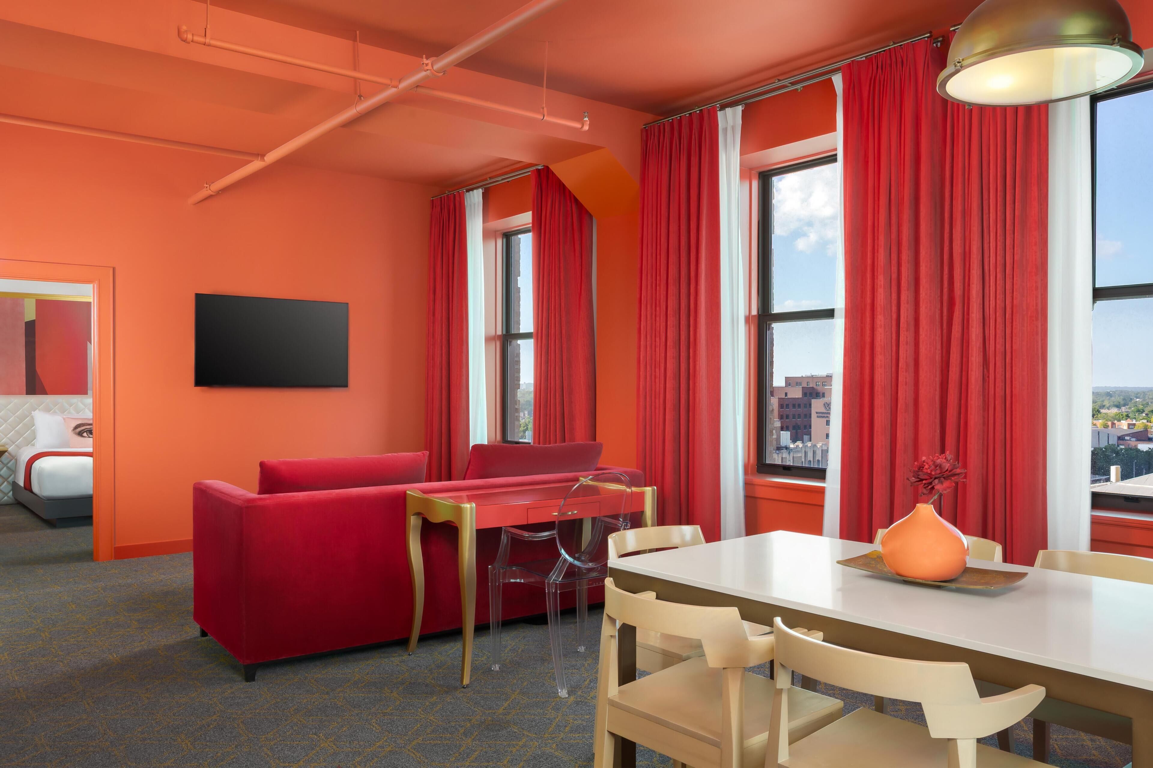 A hotel room with a red sofa, a dining table, and a city view.