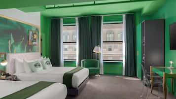 Habitación de hotel con dos camas, una silla verde, un escritorio y un ventanal con cortinas.
