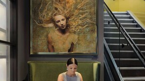 A woman sitting on a green sofa in a modern lobby with a staircase and a large framed artwork on the wall. - Angad Arts Hotel St. Louis, Tapestry Collection by Hilton (St. Louis)
