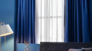 A bedroom with a bed, a window with blue curtains, and a lamp.