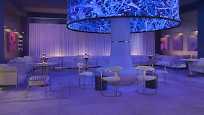 A modern lounge area with a central cylindrical light fixture, white seating, and artwork on the walls. - Angad Arts Hotel St. Louis, Tapestry Collection by Hilton (St. Louis)