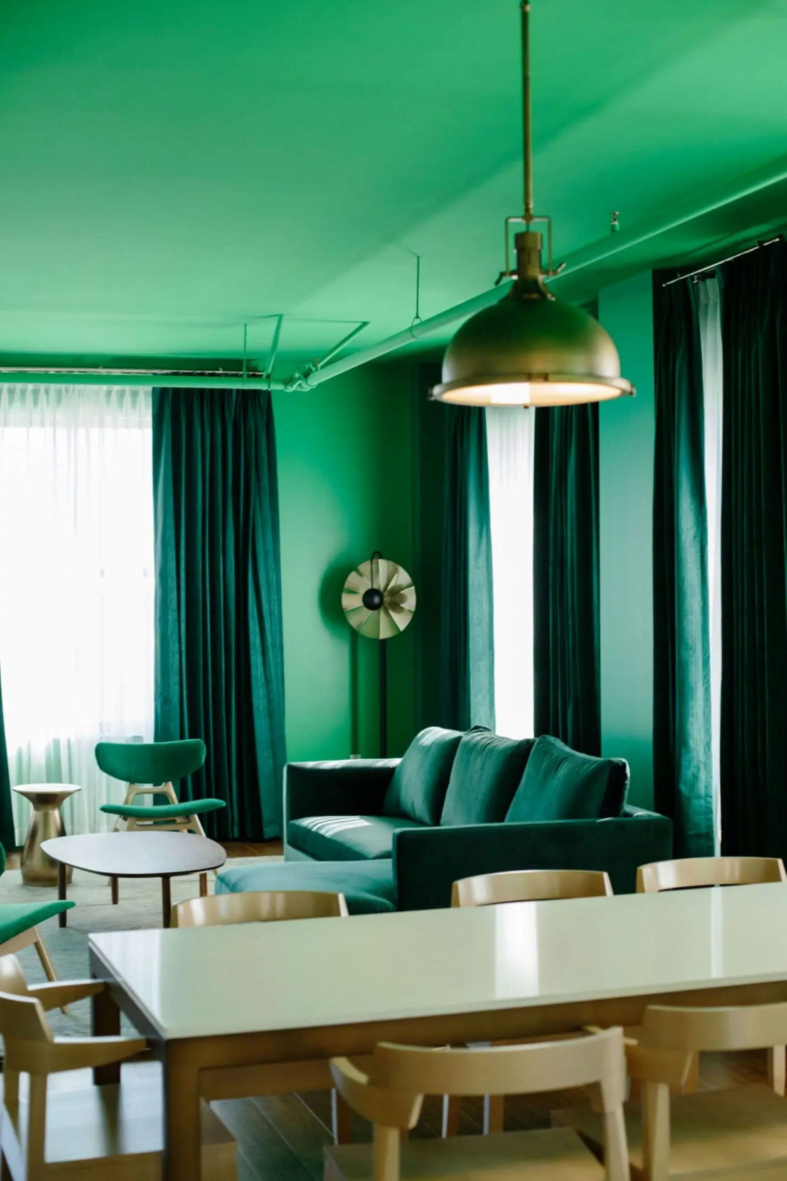 A room with a green color scheme, featuring a dining table with chairs, a sofa, and a round table with chairs.