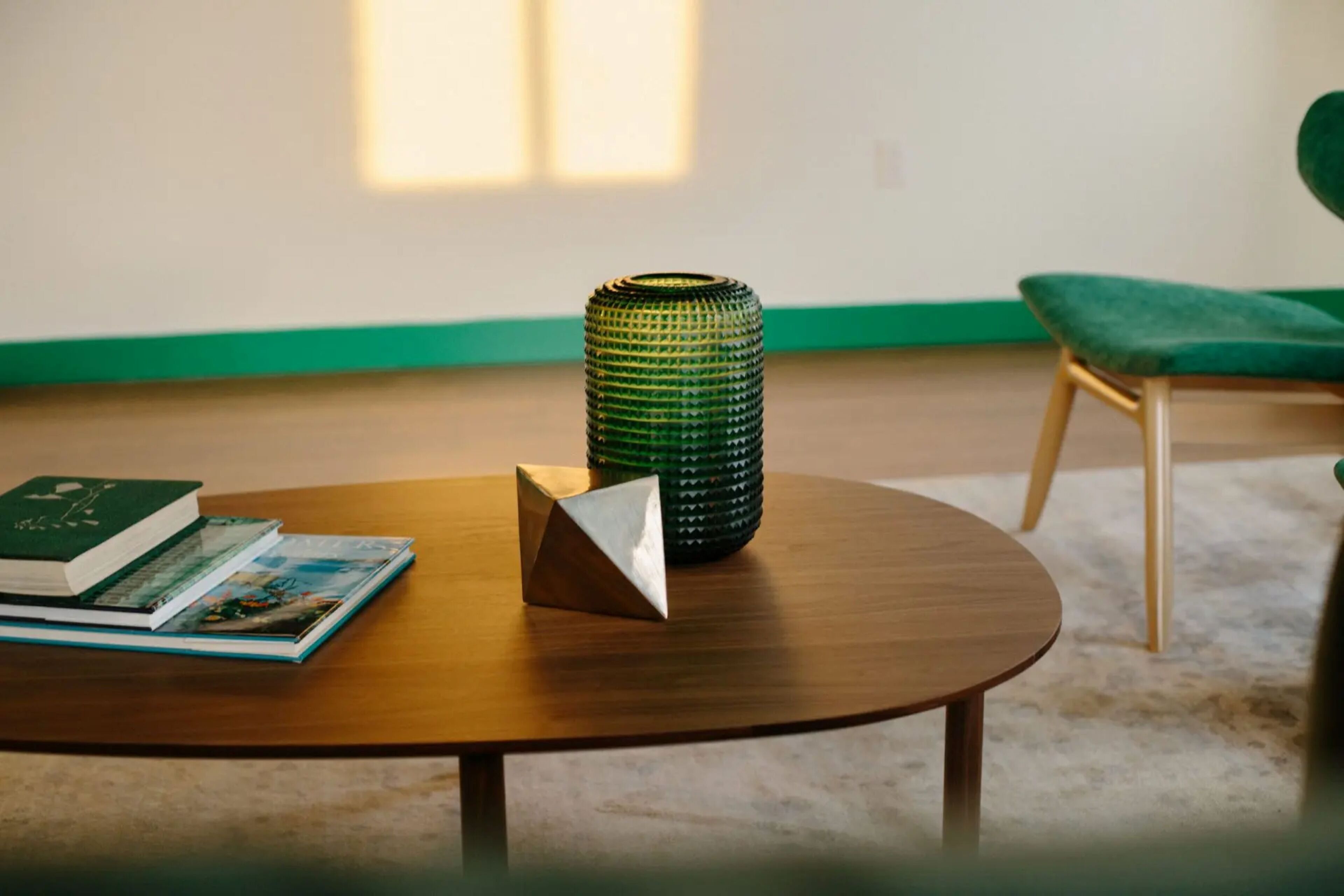 Una mesa redonda de madera con una pila de libros y un jarrón verde con textura.