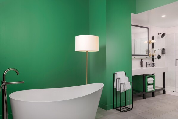 A modern bathroom with a freestanding bathtub, a large mirror, and a green accent wall. - Angad Arts Hotel St. Louis, Tapestry Collection by Hilton (St. Louis)