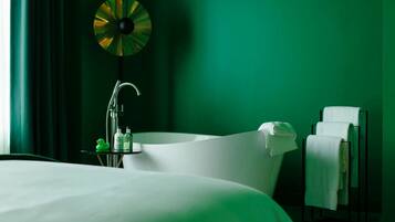 Una habitación de hotel moderna con una cama grande, una bañera independiente y un perchero para toallas.