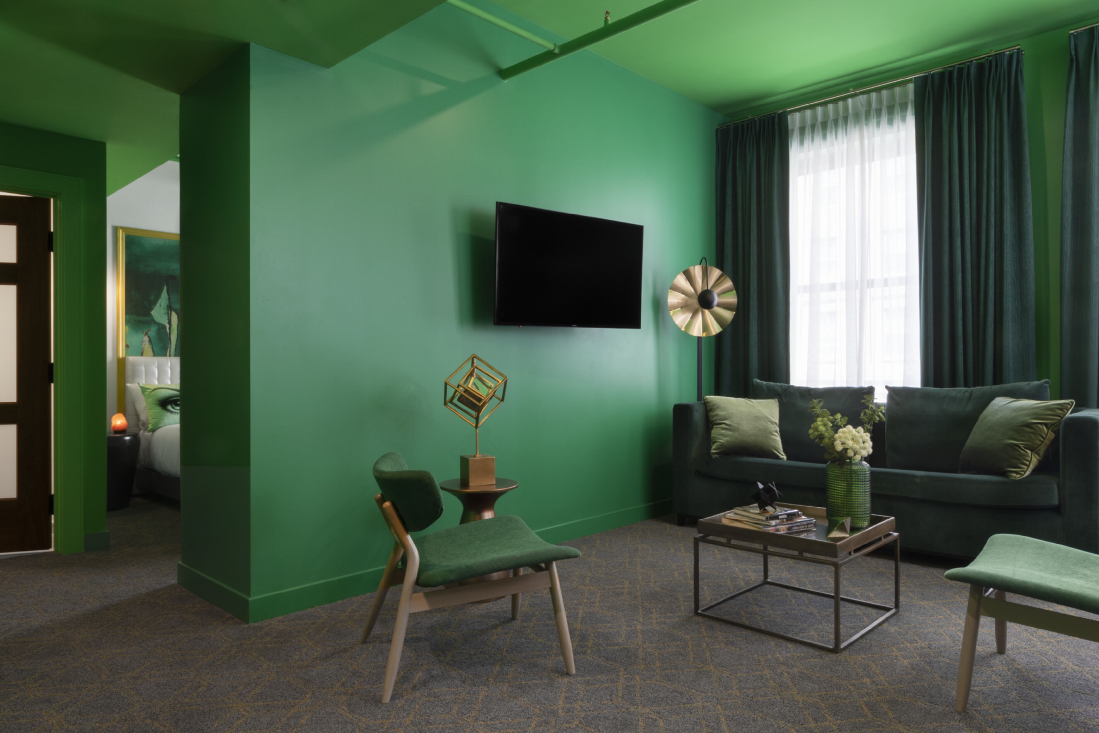 Un salon avec un mur vert, un téléviseur à écran plat, une table basse et un canapé avec des coussins.