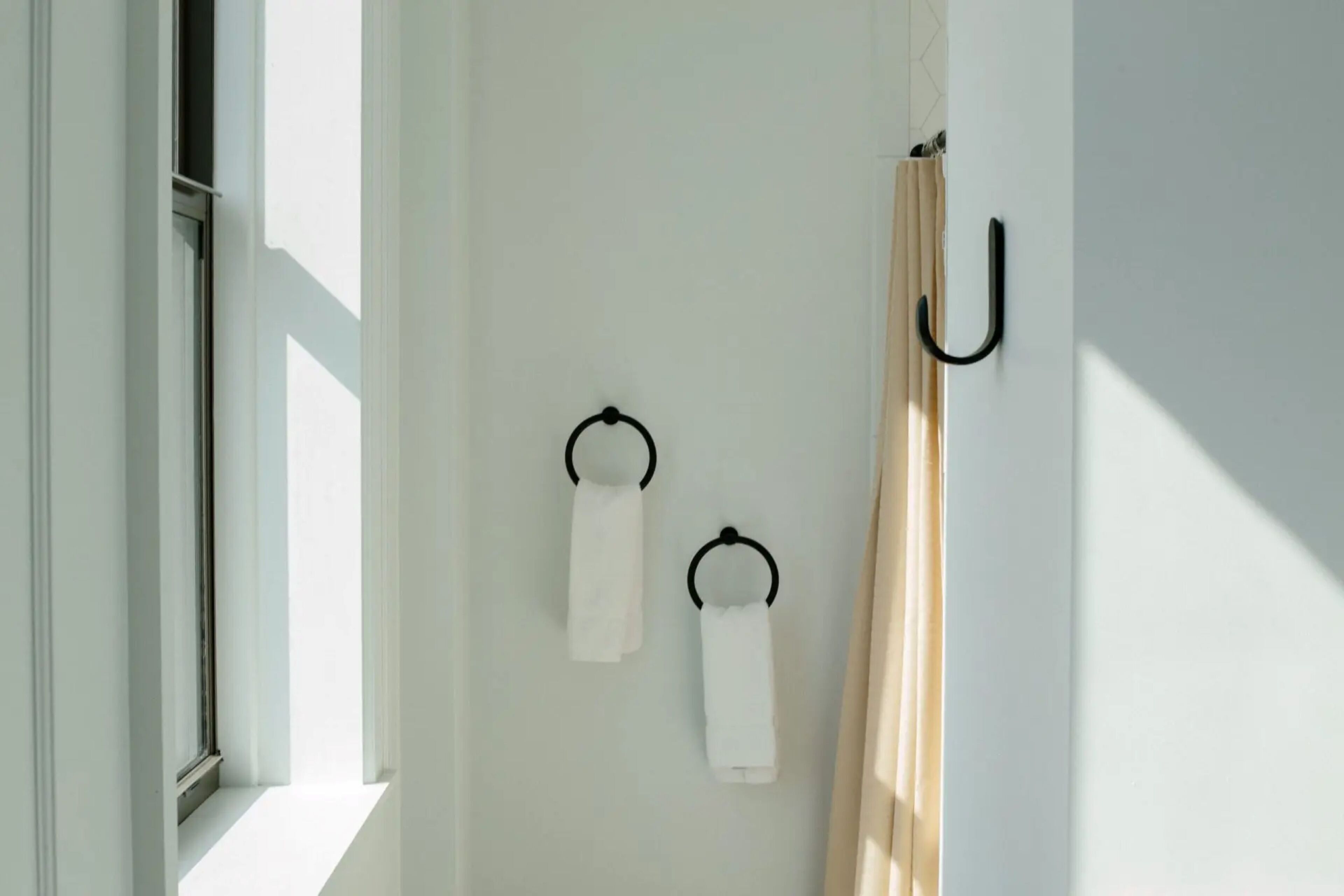 Un baño con ventana, un perchero con dos toallas y una cortina de ducha.