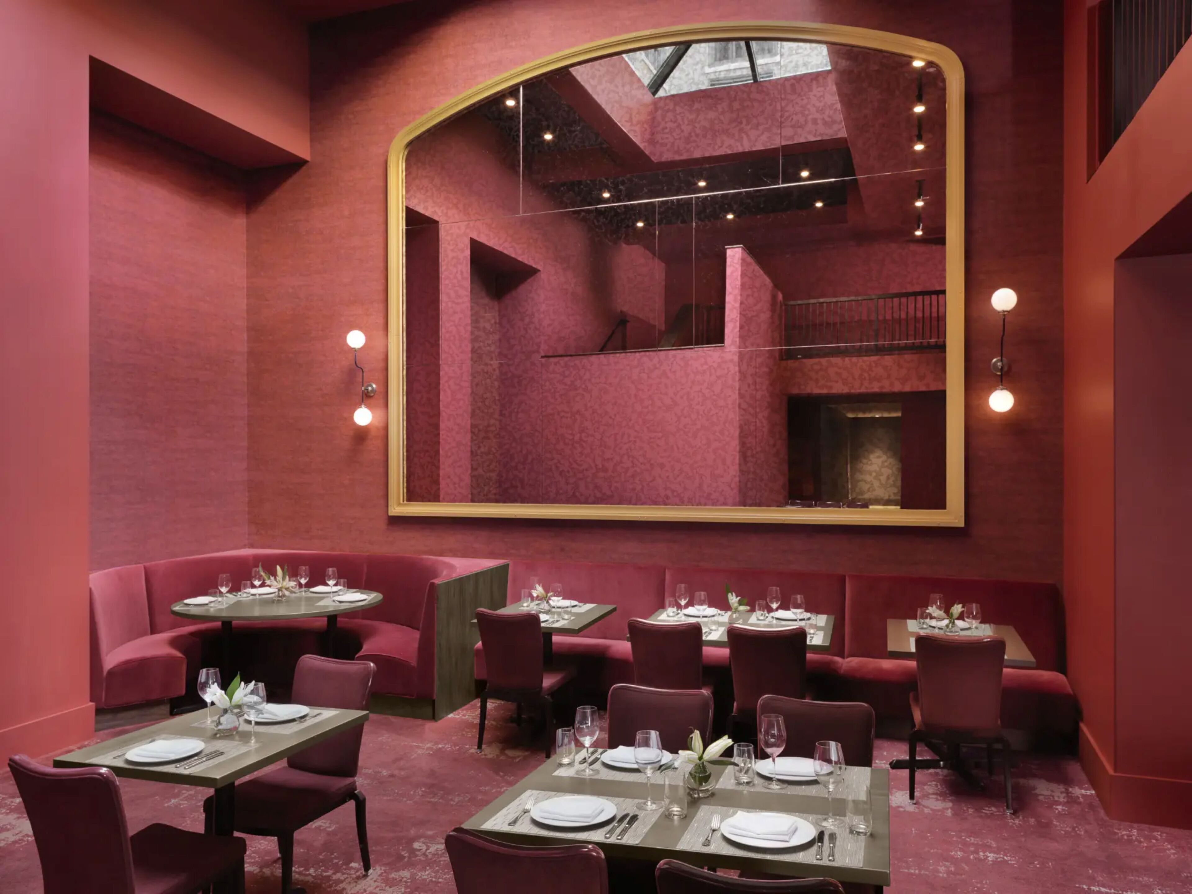 A restaurant with red walls, a large mirror, and multiple dining tables.