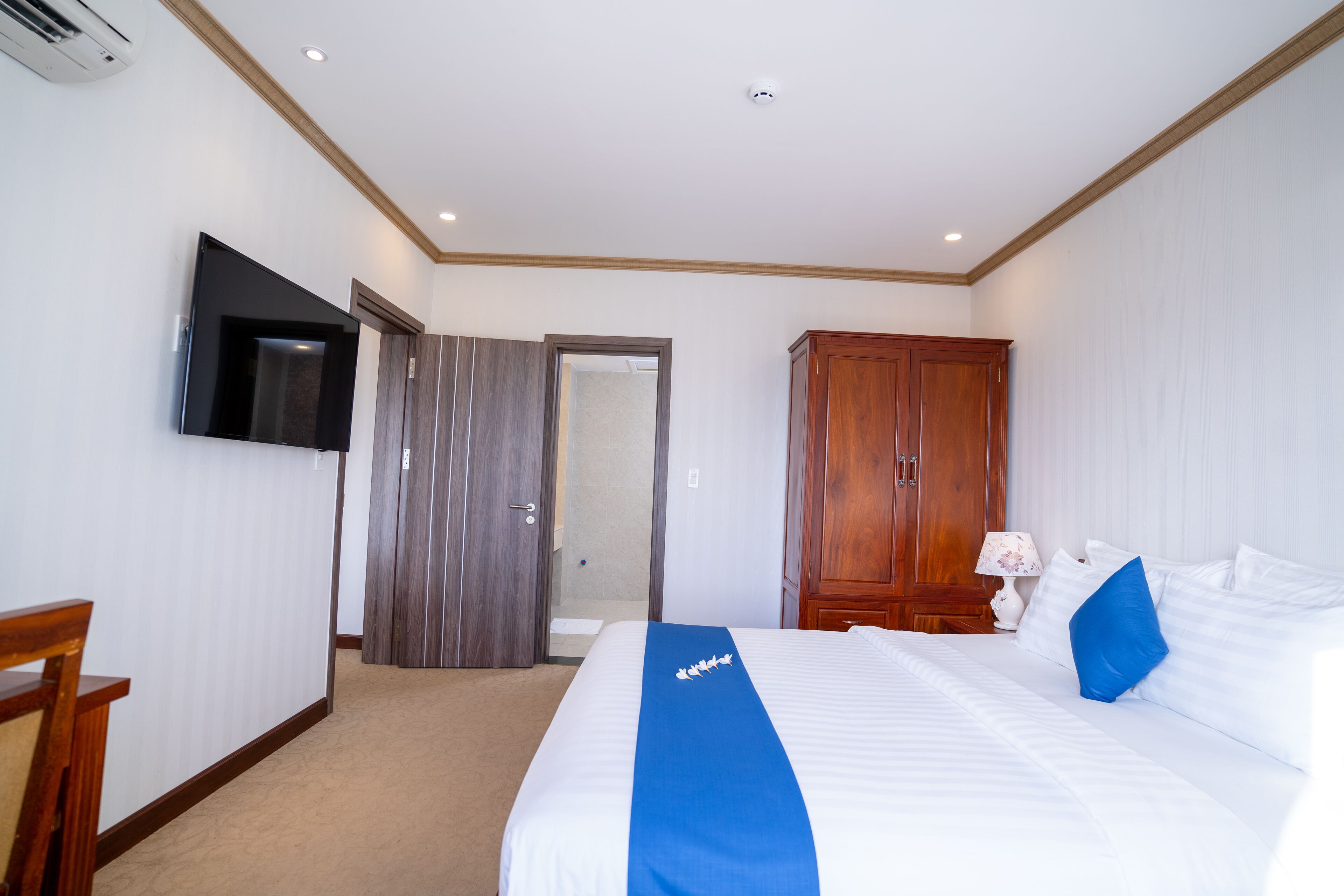 Habitación de hotel con una cama grande, un televisor de pantalla plana montado en la pared, un armario de madera y una puerta que da a un baño.